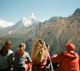 Group of trekkers sitting on a hillside, enjoying panoramic views of the snow-capped Himalayan mountains on a sunny day, representing the best trekking in Nepal.